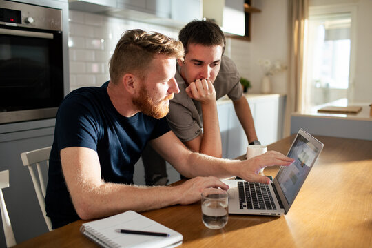 Two men reviewing finances on laptop at kitchen table