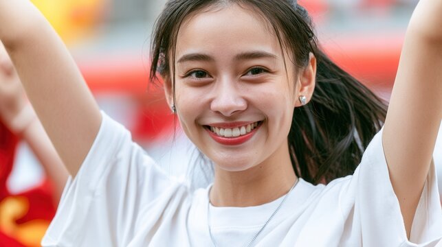 Enthusiastic young asian female sports fan cheering with arms raised.