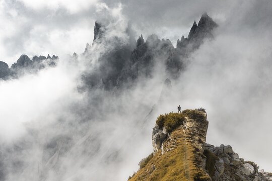 Man standing on a ridge, behind mountain tops, rocky ridge with sharp rocky peaks, dramatic clouds, Cimon di Croda Liscia and Cadini group, Sesto Dolomites, Belluno, Italy