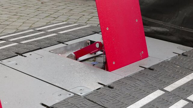 Retractable vehicle barrier rising from street pavement. Red automated rising arm barrier emerging from the ground as an anti-terrorism security measure to control vehicle access