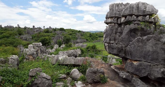 Scenic mountain path leads toward famous mushroom shaped rock formation known as Wannian Lingzhi in Shilin Stone Forest. Camera pans right from distant horizon peaks to reveal massive boulder