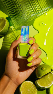 Hand holding lime green nail polish bottle on a vibrant citrus background.