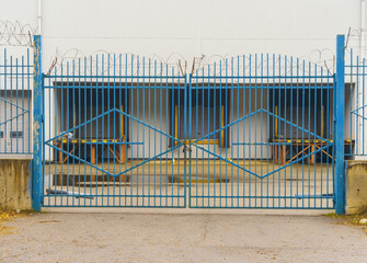 Roaring gate surrounds empty lot. Industrial premises barricaded with security measures and overcast sky © ossyffer