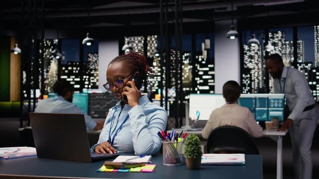 African american woman answering phone call for a briefing discussion, using laptop and requesting assistance. Manager does research on profitability, telephone call in office.