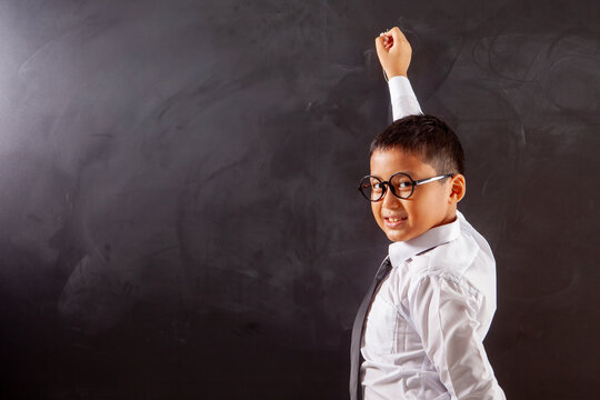 Smiling Schoolboy with Glasses Writing High up on Chalkboard with Copy Space