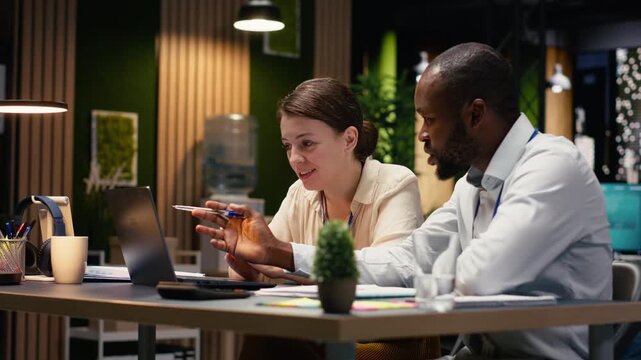 Evaluating operational metrics, laptop and team of businesspeople at office desk. Colleagues working late at night, teamwork in assisting online clients and finishing tasks on notebook.