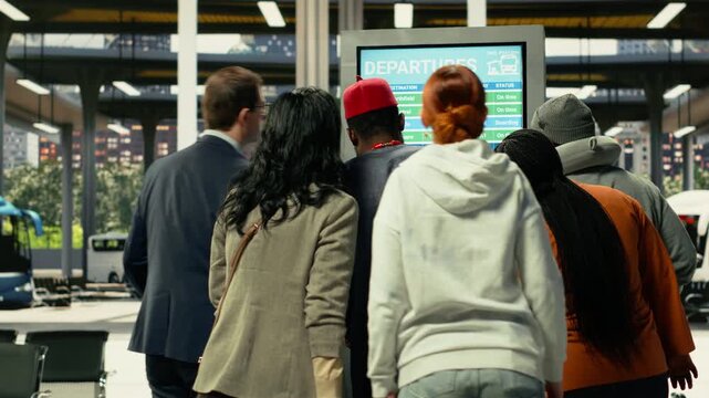 Flow of travelers moving through busy coach station during departure hours. Diverse passengers with baggage monitoring timetable and schedule on screen, long-distance bus travel.