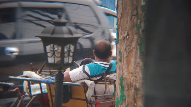 PAMEKASAN, INDONESIA - JANUARY 05, 2026: Authentic footage of a traditional Indonesian pedicab driver, known as Tukang Becak, resting and snacking on his vehicle by a busy city roadside. Relaxing