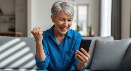 Fototapeta premium Happy older woman celebrates good news on her phone