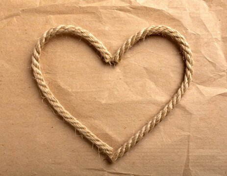 Heart shape made of rustic jute rope on textured brown kraft paper, symbol of love and romance, rustic wedding invitation element
