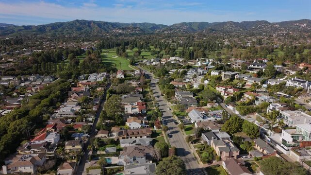 Aerial view los angeles suburb morning, panoramic neighborhood with treelined streets, diverse residential roofs, swimming pools, manicured lawns, golf course fairways, foothill backdrop,