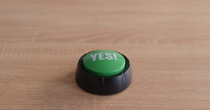 On a wooden desk, hand presses green yes button to signal approval, confirm intent, and finalize a choice or decision. A hand presses a green yes button. Concept of pressing, accept and solution.