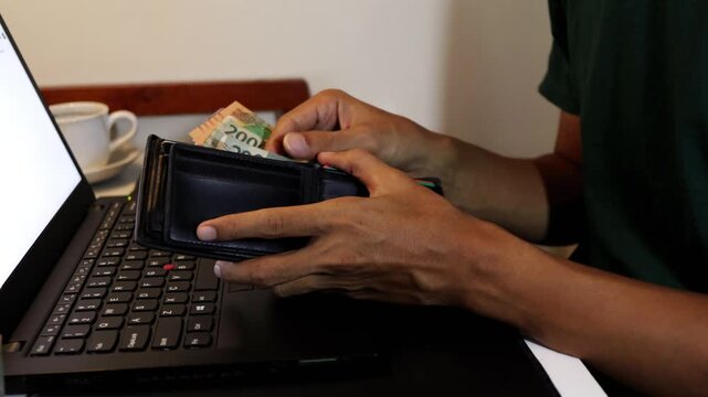 Unrecognizable Indonesian man checking cash money from his wallet at a work desk.