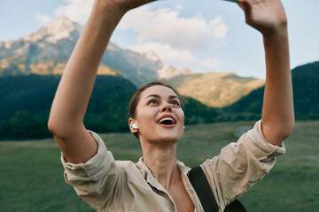 Fototapeta premium Joyful brunette woman raises her arms in a sunlit mountainside meadow, capturing a moment of outdoor adventure, freedom, and positive energy in the open air.