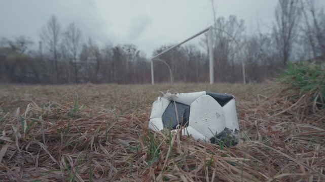 Deflated Torn Soccer Ball Lying on Abandoned Overgrown Football Field | Wide-Angle Ground-Level Parallax | Urban Decay and Neglect Concept