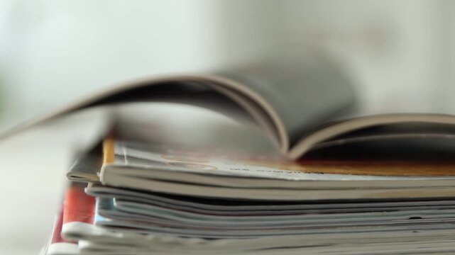 Many lifestyle magazines on table indoors, closeup. Camera moving up