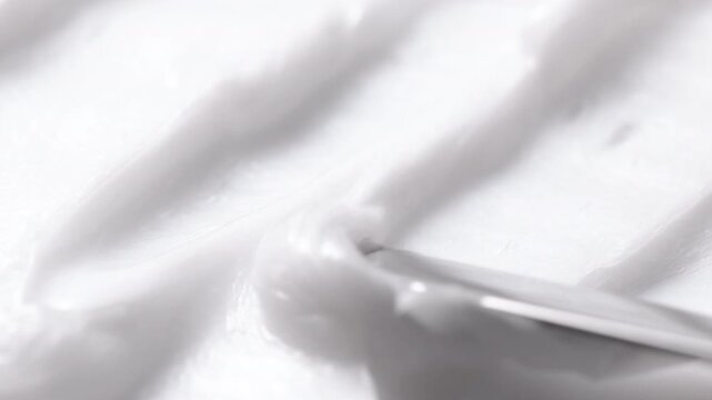 Close-up of white cosmetic cream texture being smoothed with a spatula