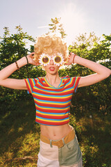 A woman in a striped top poses outdoors in bright sunlight, wearing large daisy sunglasses. Retro...