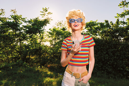 A smiling woman outdoors wearing a striped crop top and sunglasses in sunny park, capturing a casual retro lifestyle. Bright colors and warm light evoke vintage film tones.