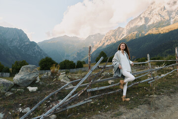 Fototapeta premium Cheerful woman outdoors, smiling in mountain landscape, casual chic pose, sunlit moment, natural colors, relaxed lifestyle, scenic backdrop with dramatic peaks,glow