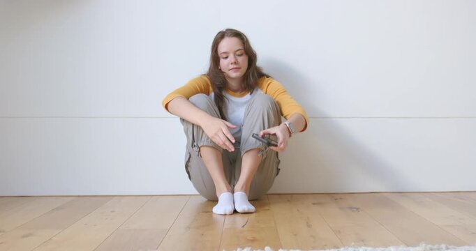 Female in white tee wearing smartwatch spotting phone on hardwood floor, picking up to check