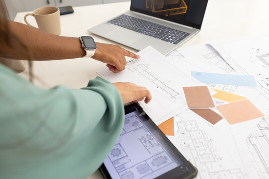 Diverse female designers leaning at studio reviewing plans with tablet tan swatches light green top