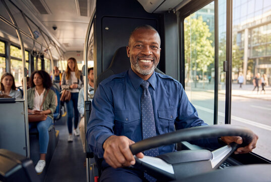Smiling african american bus driver in blue uniform driving city bus with passengers inside.