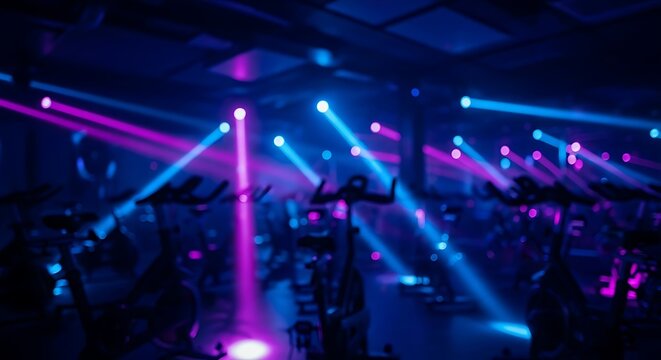 Spinning class studio with blue and pink lights and exercise bikes in a dark room, blurred motion effect