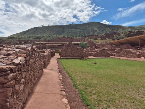 Inside ancient ruins with red rock walls, green grass, and protective shelter roof