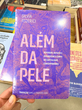 BELO HORIZONTE, MG, BRAZIL, MAY, 10, 2026 A hand holding a purple book titled Alem da Pele by Silvia Federici in a bookstore