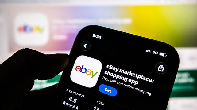 Closeup of a hand holding a smartphone displaying the ebay marketplace shopping app on the screen