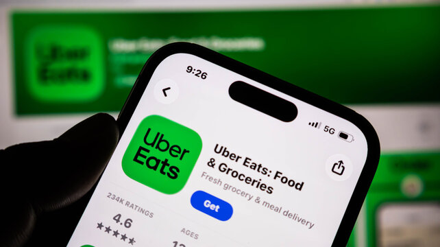 Closeup of a hand holding a smartphone displaying the uber eats app store page on a screen