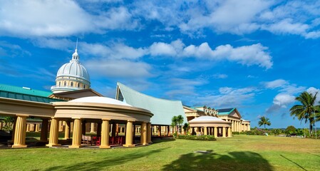 Panoramic view of the Palau National Capitol complex in Ngerulmud, Melekeok State, with its dome, columns, and distinctive rooflines framed by palm trees and blue skies © Leonid Andronov
