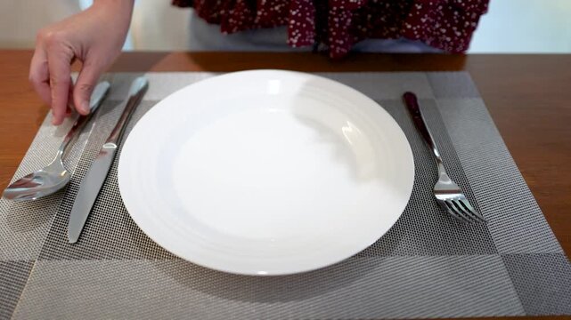 Person Setting a Dining Table with White Ceramic Plate and Silverware