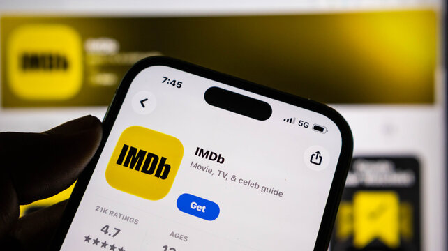 Closeup of an iphone screen displaying the imdb app store page with the download button visible, held in a persons hand