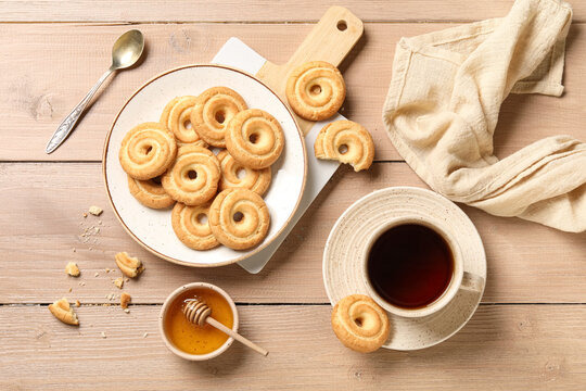 Plate with tasty spritz biscuits and cup of tea on beige wooden background