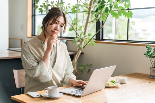 A young Asian woman is thinking about her work remotely while eating at a cafe.