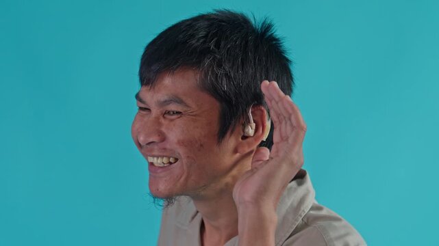 Cheerful Young Man Smiling And Gesturing To Listen While Wearing Modern Hearing Aid Device