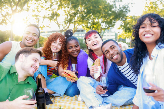 Group of friends holding red wine glasses at picnic party - Happy young people having fun drinking and eating healthy food together
