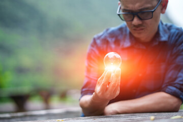 Man Holding Glowing Light Bulb Against Green Nature Background © aekachai