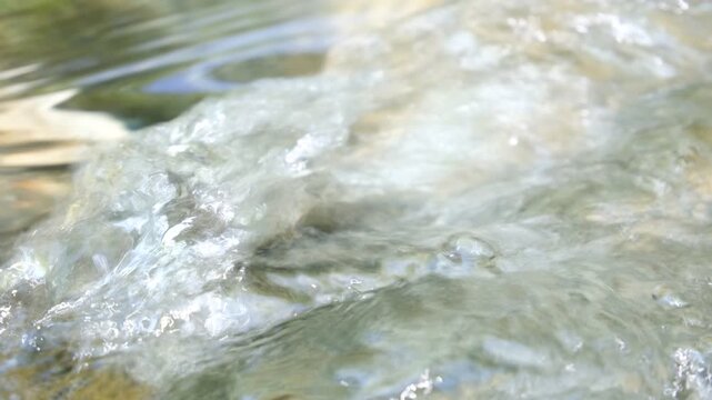 Clear mountain stream water rushing with bubbles and sparkling reflections