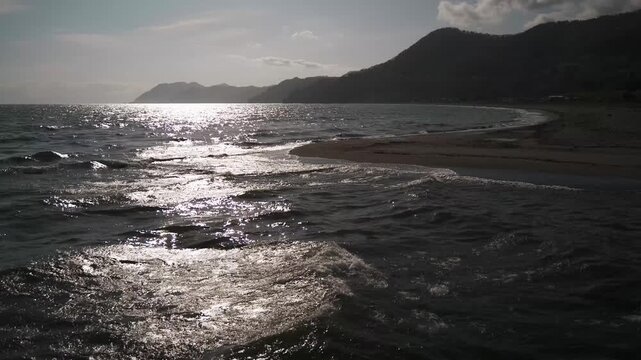 A sandbar at a river mouth flowing into a bay, with the silhouette of distant mountain ranges in the background.