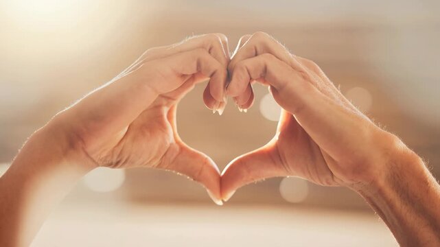 Close up of two hands forming a heart shape symbol with soft warm light background for love and friendship concept