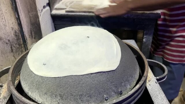 A professional dhaba chef tossing and stretching a paper-thin rumali roti over a traditional hot inverted iron tawa at a roadside eatery in India.