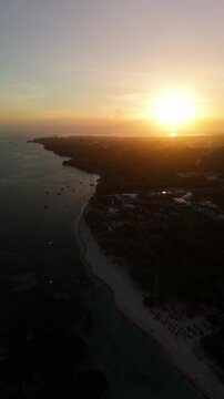 Drone descends over Panglao at sunset with silhouetted coastline, beach, and calm coastal water