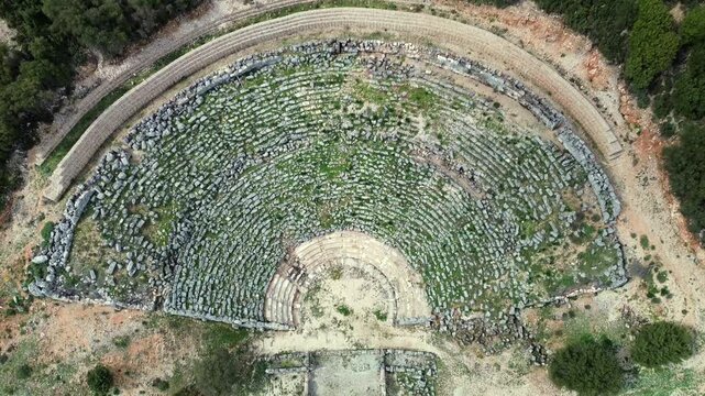 Stunning 4K drone top-down view over the ancient Greek theater in Kassope, Greece. Symmetrical abstract landscape of stone cavea rows, semicircle orchestra and archaeological layout.