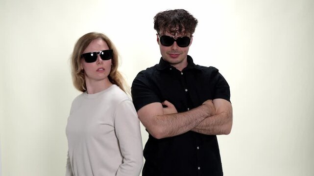 A playful couple wearing sunglasses poses against a clean white background, embodying concepts of fun, love, and modern relationships. This studio shot captures their joyful expressions and casual sty