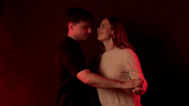 Romantic connection and intimacy are depicted as a young couple holds hands and gazes into each other s eyes, illuminated by a soft red light against a dark background. This scene evokes feelings of l