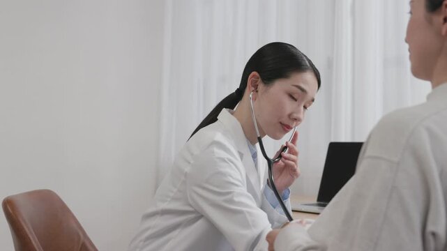 Asian Female Doctor Using Stethoscope to Examine Female Patient