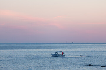 Obraz premium A small timber fishing boat hauling in fishing equipment at dusk on the mediterranean coast